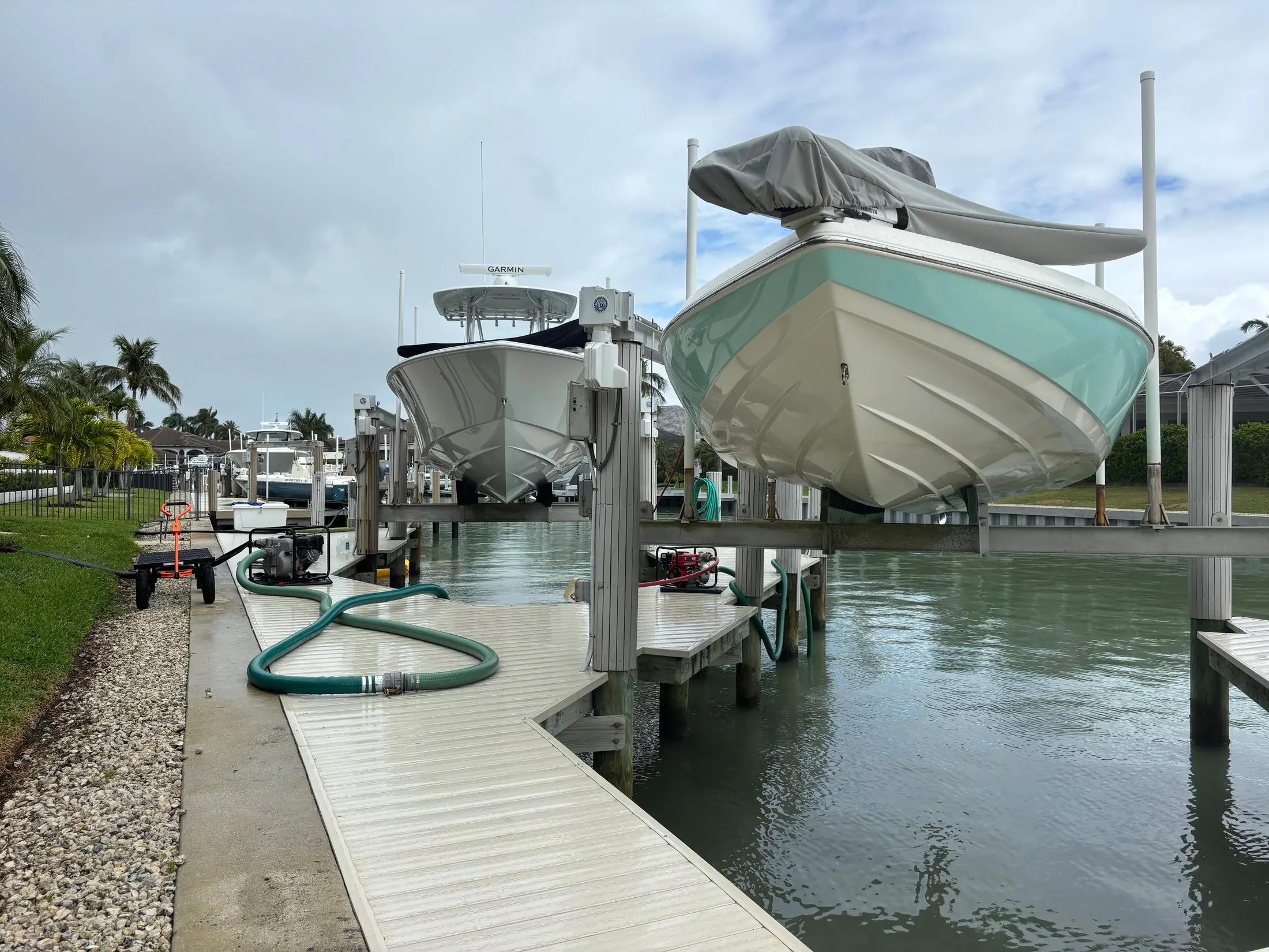 Dock & Dredge: boats raised on lifts beside a dock with a hose along the walkway