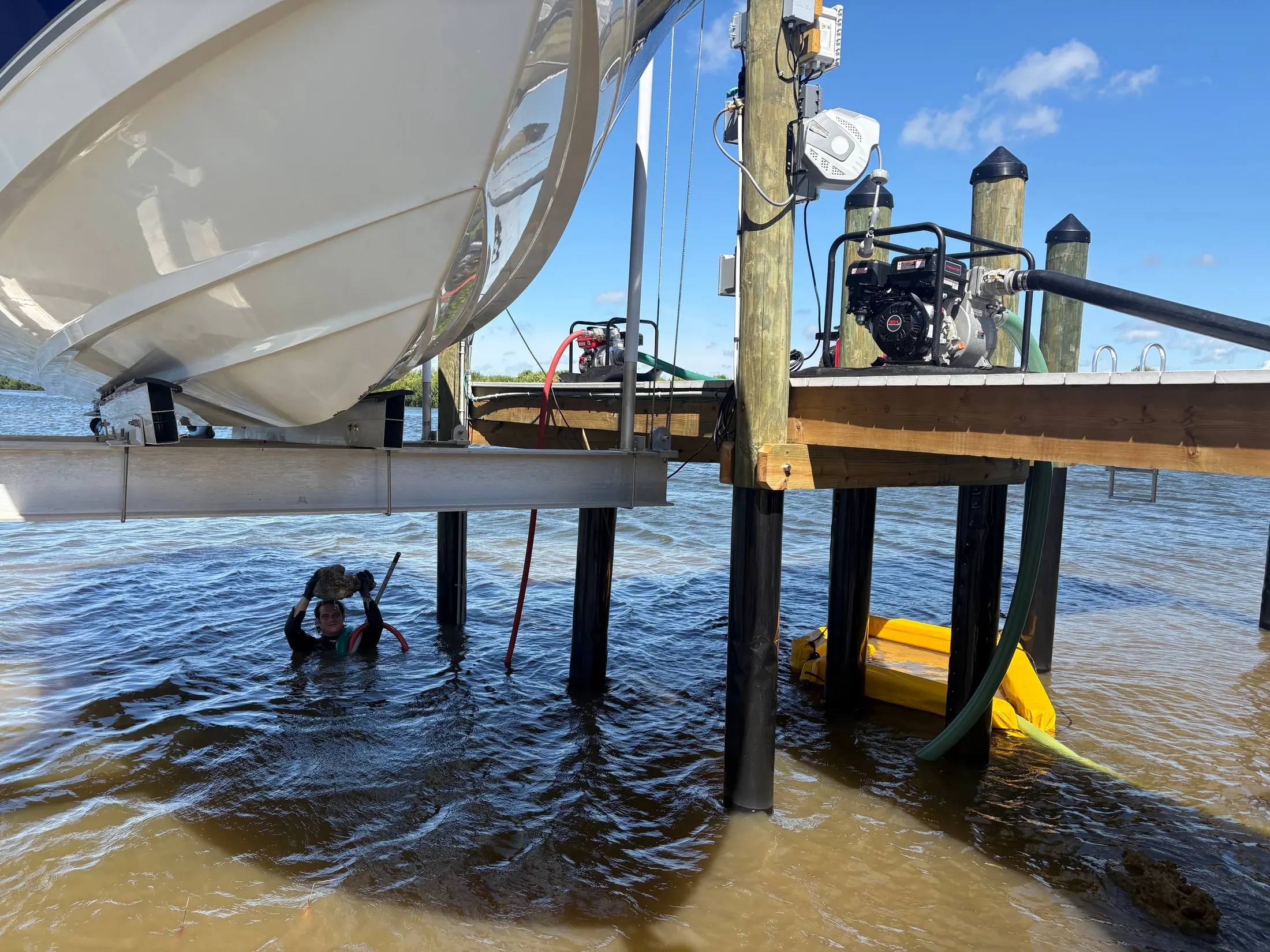 Dock & Dredge: worker in the water beside a dock with pump and hose equipment