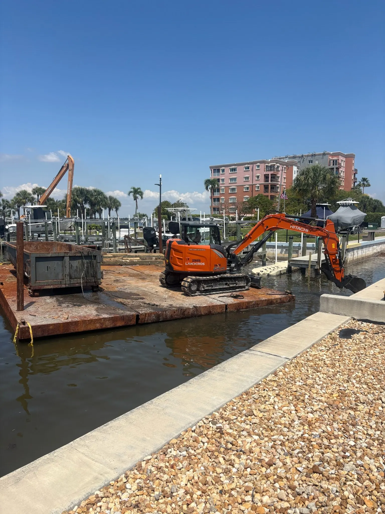 Dock & Dredge: excavator on a floating platform beside a waterfront dock